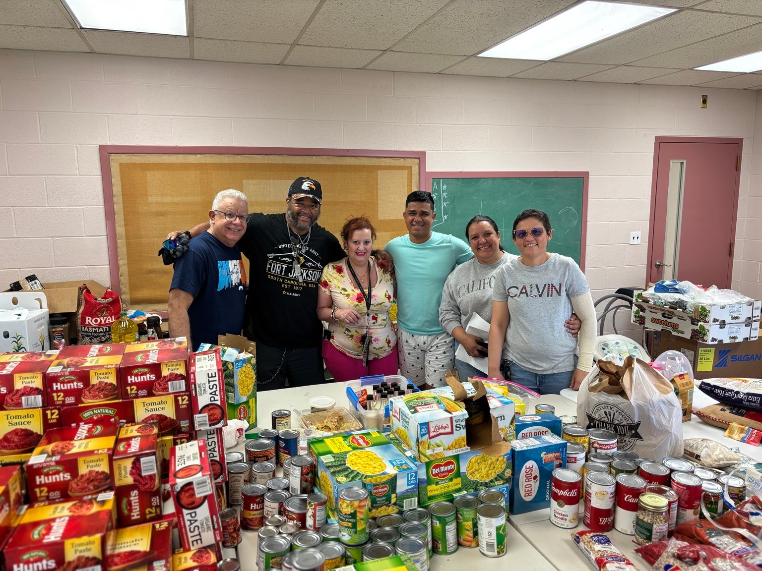 Community members surrounded by pantry food and household supplies